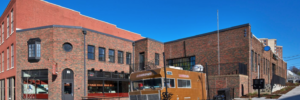 Exterior corner view with food truck on patio in foreground and red-brown brick two story building in background