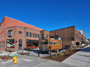 Exterior corner view with food truck on patio in foreground and red-brown brick two story building in background