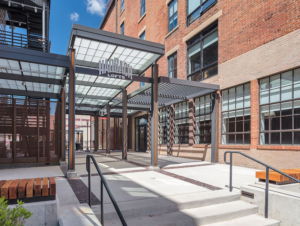 Steel framed entry canopy with red-orange brick warehouse in background