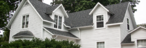 white farmhouse with gable roof surrounded by green shrubs