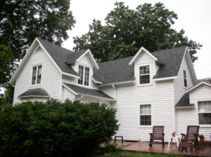 white farmhouse with gable roof surrounded by green shrubs